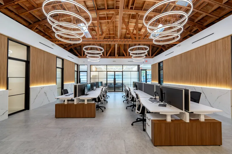 Open-plan sit-stand benching under a wood-truss ceiling, Los Angeles