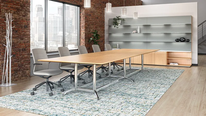 Conference room with a light wood table on polished metal bases and gray chairs in a brick-walled space, manufacturer photo